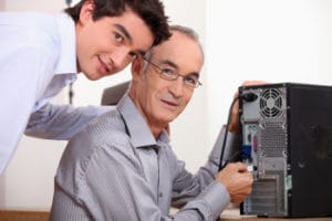 Image of a young man helping a mature man with his desktop computer, image from Shutterstock