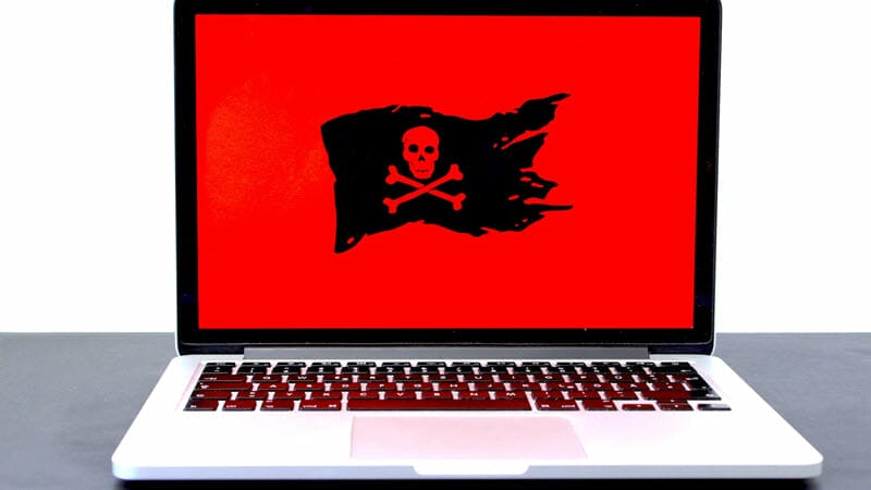 A pirate flag on a red background is displayed on a laptop.
Caption: Cyberattacks come in a variety of forms. - image licensed from unsplash.com